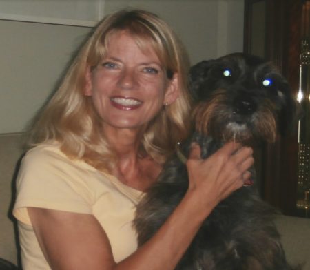 Cindy Hoppes smiling, holding a dark-colored dog close to her.